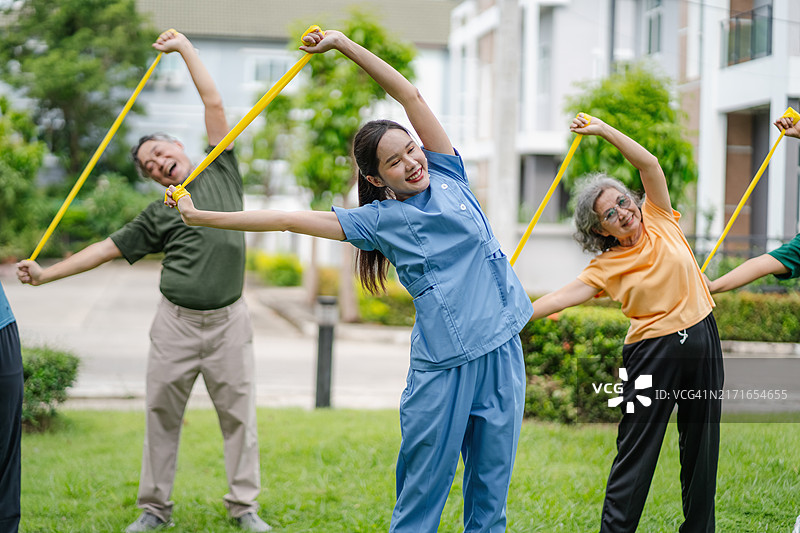 护理员带领老人们在花园里用弹力带锻炼肌肉，保健概念图片素材