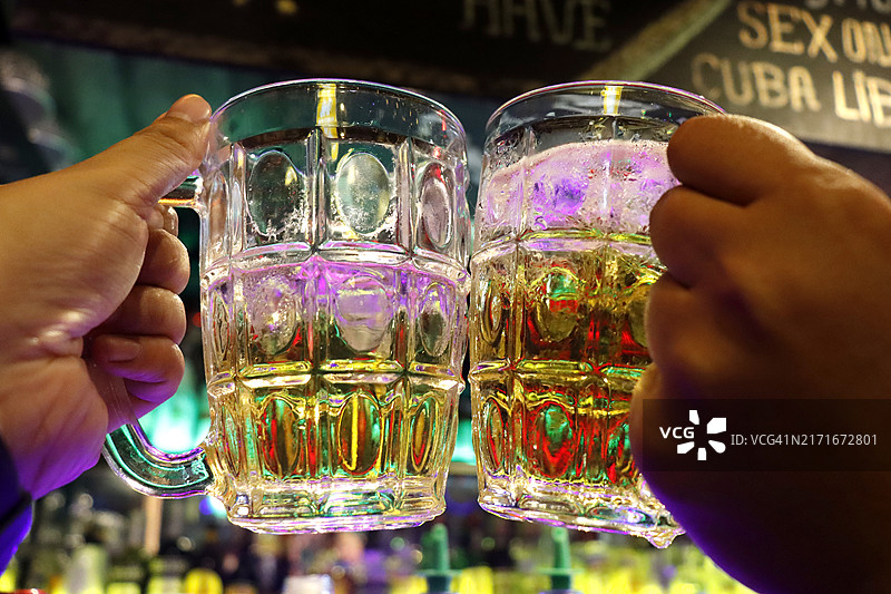 干杯！碰杯。手持啤酒杯和啤酒气泡的特写镜头图片素材