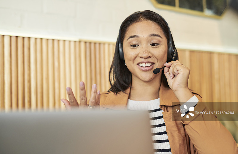 在咖啡店咨询的亚洲女性使用笔记本电脑和耳机进行远程工作。电脑、通讯和女性虚拟助手与客户预约、日程安排，在咖啡馆会面图片素材