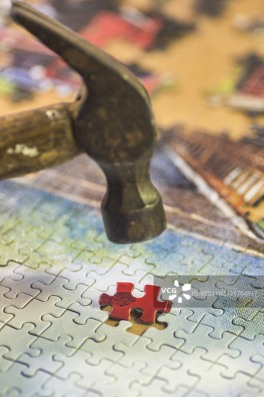 拼图碎片，完整的拼图，最后一块红色碎片已准备好但尚未放入拼图中。宏图像。锤子击打碎片。英国苏格兰中部地区图片素材