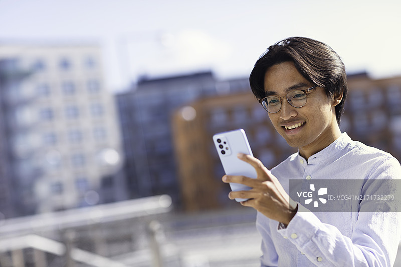 快乐的男人在办公楼外的户外使用手机图片素材