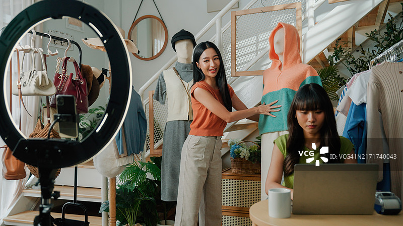 年轻的亚洲女人在直播时向顾客展示网店里的服装图片素材