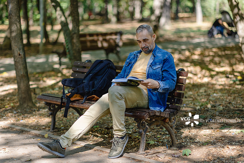 背着书包的男子在公园长椅上放松。图片素材