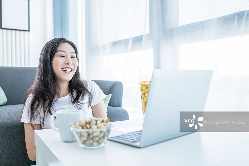 亚洲女性在笔记本电脑上看电影并吃爆米花图片素材