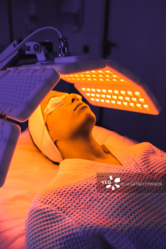 女病人在现代豪华美容诊所接受橙色LED灯或RLT疗法，进行皮肤再生。图片素材