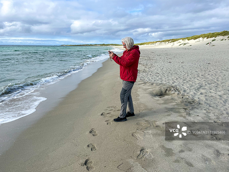 在海滩上用手机拍照的戴眼镜的年长女性图片素材