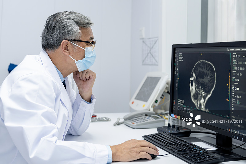 亚洲老年医生在电脑桌前观看患者进入MRI扫描仪图片素材