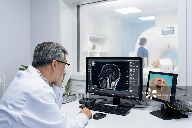 亚洲老年医生在电脑桌前观看患者进入MRI扫描仪图片素材