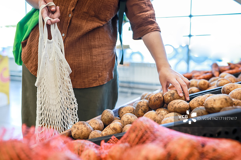 有意识的消费：少女选择有机带泥土的土豆，并使用可重复使用的棉布袋，强调环保购物图片素材