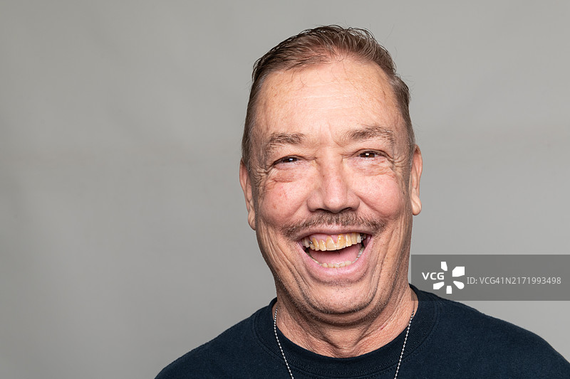 在灰色背景下，快乐的老年男人笑着看着镜头图片素材