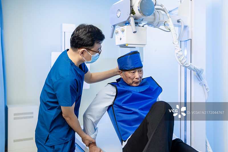 亚洲放射科医生为老年男性患者穿上防护服，准备进行X光检查图片素材