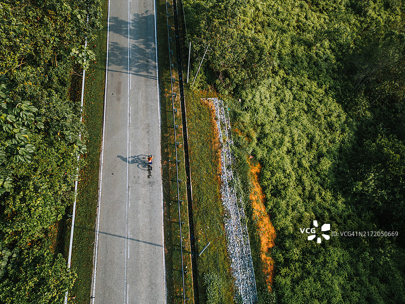 在乡村地区的自行车公路旅行，早晨无人机视角下的女运动员骑手与长长的阴影图片素材