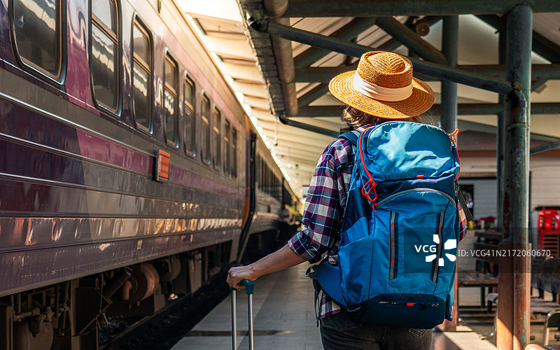 在火车站行走的女游客。年轻的亚洲女游客背着背包，拖着行李在铁路上。积极的旅行生活方式概念图片素材