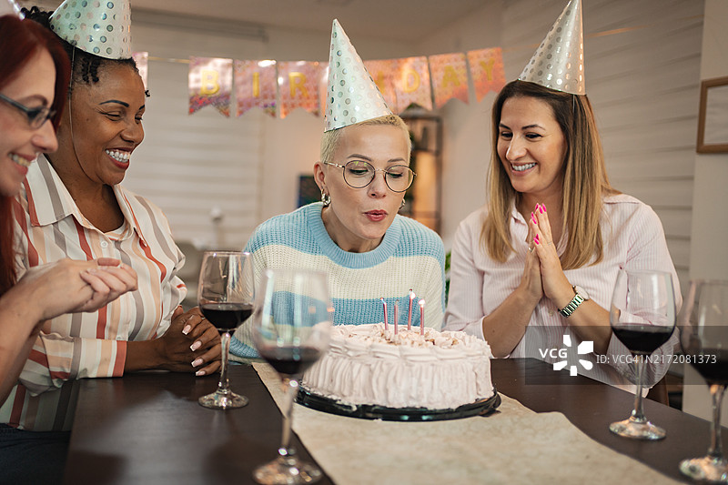 四个快乐的女人庆祝40岁生日，有蛋糕和派对帽图片素材