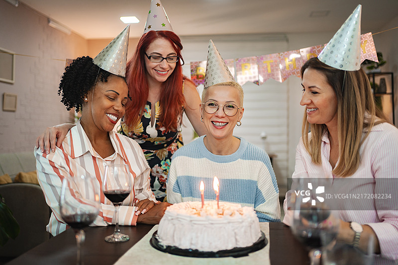 四位妇女在舒适的聚会上，戴着节日帽，欢笑着庆祝40岁生日图片素材