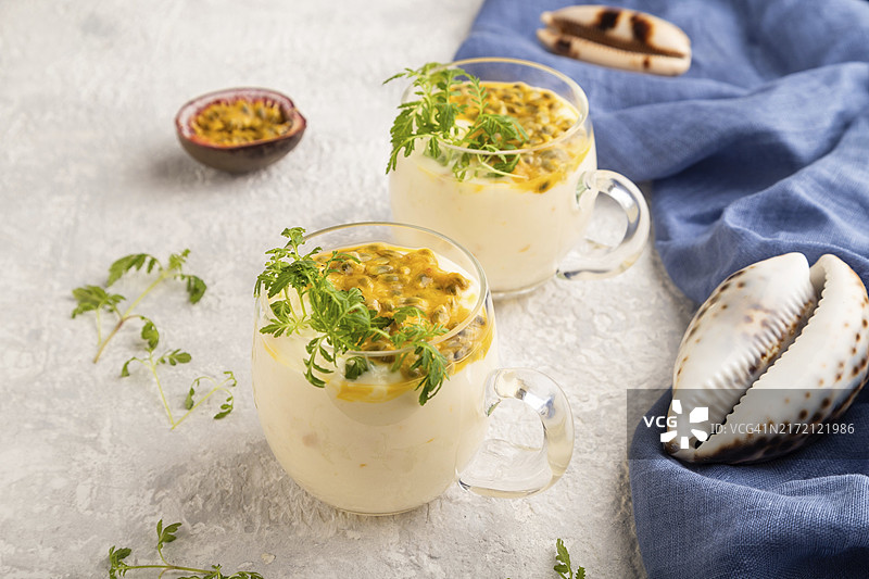 灰色水泥背景下玻璃杯中的百香果和万寿菊苗酸奶，搭配蓝色亚麻纺织品。侧视图，特写图片素材