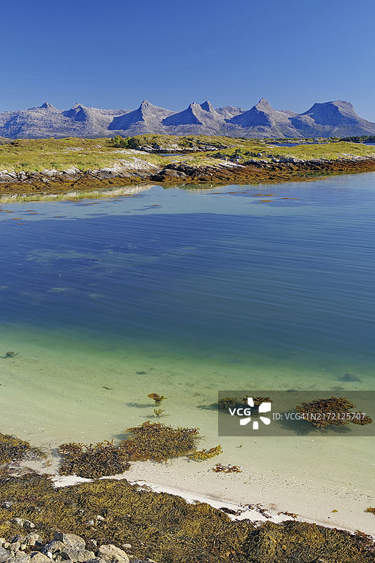 平静清澈的峡湾，有海藻、白色沙滩和山脉，背景是明亮的蓝天，七姐妹山脉，阿尔斯塔豪格，诺尔兰，挪威，欧洲图片素材