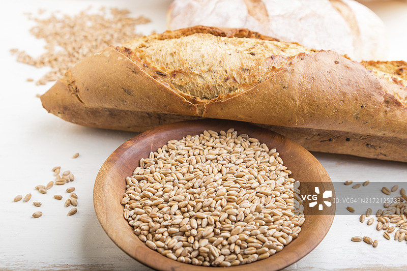 新鲜出炉的面包和小麦种子木盘，白色木质背景图片素材