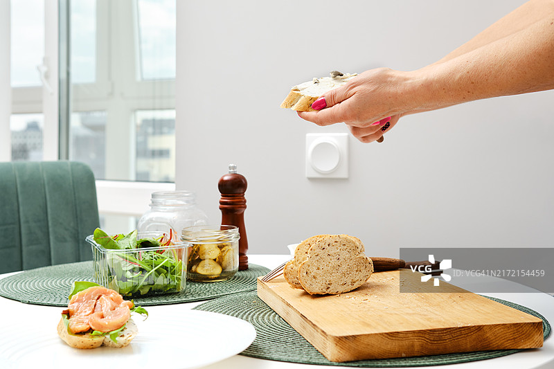 在三明治上涂抹奶油奶酪的匿名女人的手图片素材