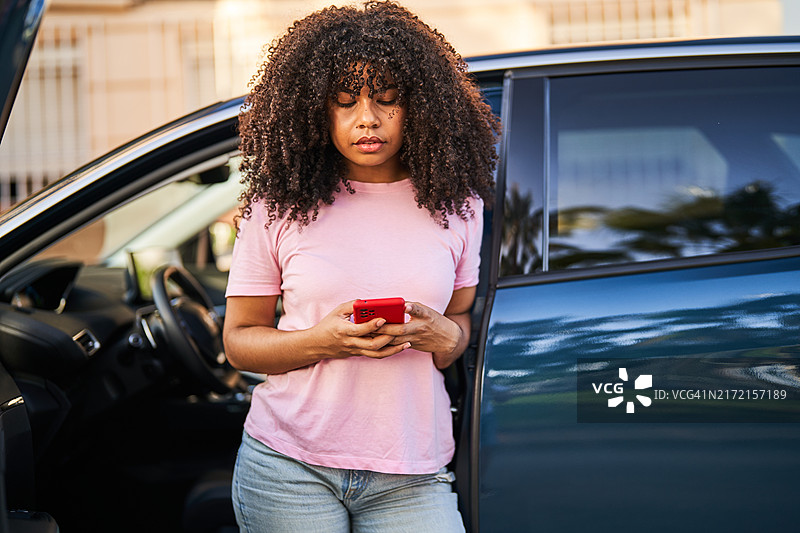 靠在电动汽车门边使用智能手机的年轻女人图片素材