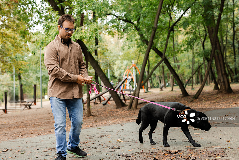 年轻男子与唐氏综合症在悠闲地遛狗图片素材