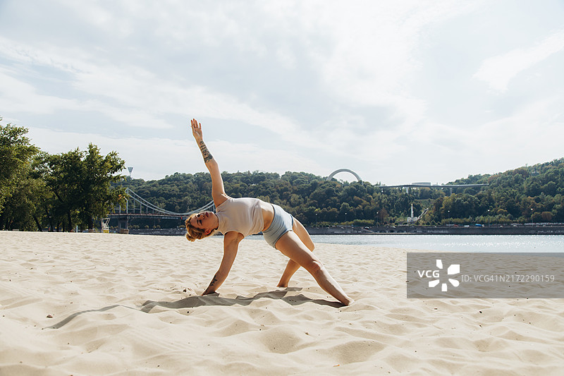 纹身年轻女人在城市海滩练习瑜伽图片素材
