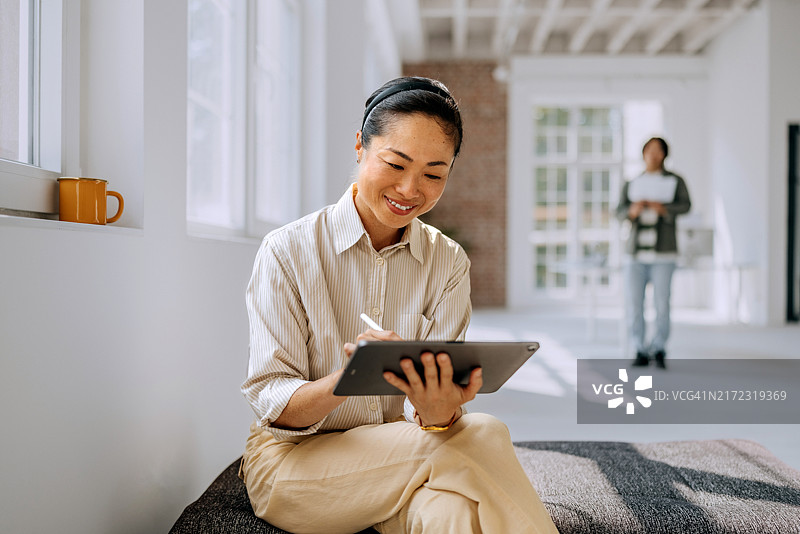 在现代办公室放松时使用平板电脑的微笑女商人图片素材