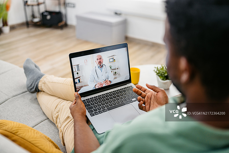 年轻男人在沙发上用笔记本电脑预约医生图片素材