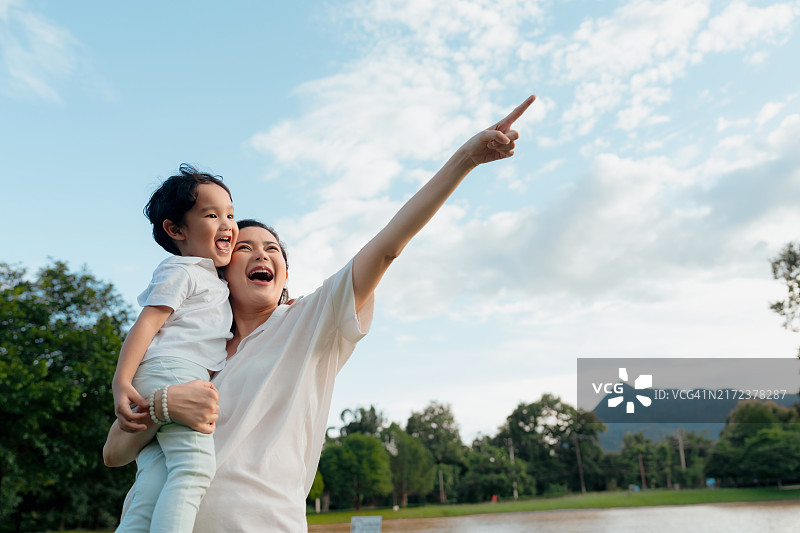 阳光明媚的日子里，母亲紧紧地抱着儿子，在户外享受美好时光。母亲温暖地笑着，捕捉到了温馨有爱的家庭瞬间图片素材