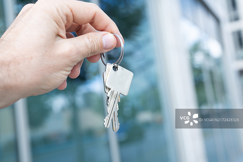 一个人站在现代办公大楼前，手中拿着钥匙。图片素材