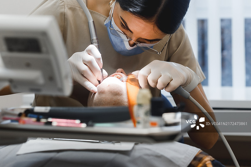 女牙医为病人治疗牙齿。医生是女人，顾客是男人。在医疗办公室工作图片素材