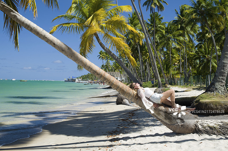 年轻女游客躺在巴西卡内罗斯海滩的椰子树下，巴西，南美洲图片素材