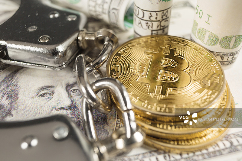 戴着手铐的美元纸币上的金色比特币加密货币：数字犯罪、逮捕或黑客概念图片素材