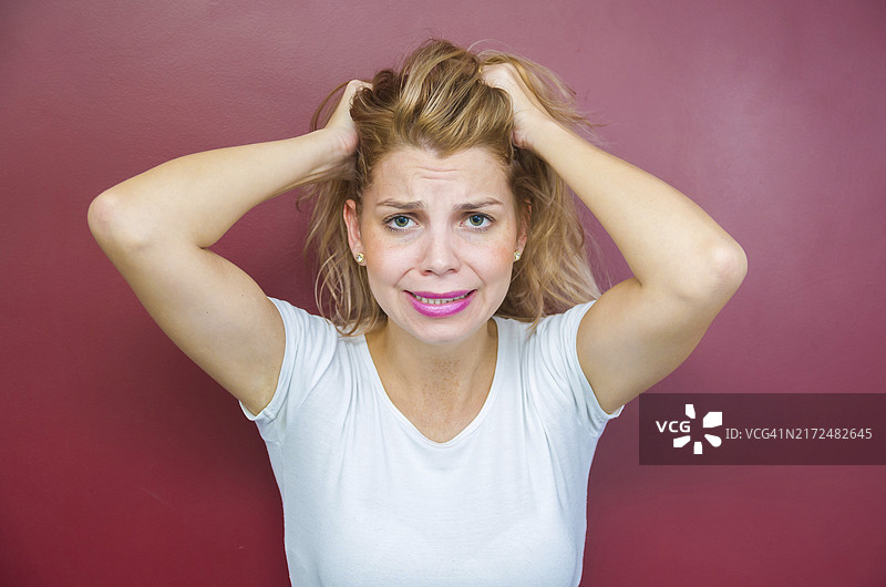 忧虑的概念：双手抱头的红背景女子图片素材