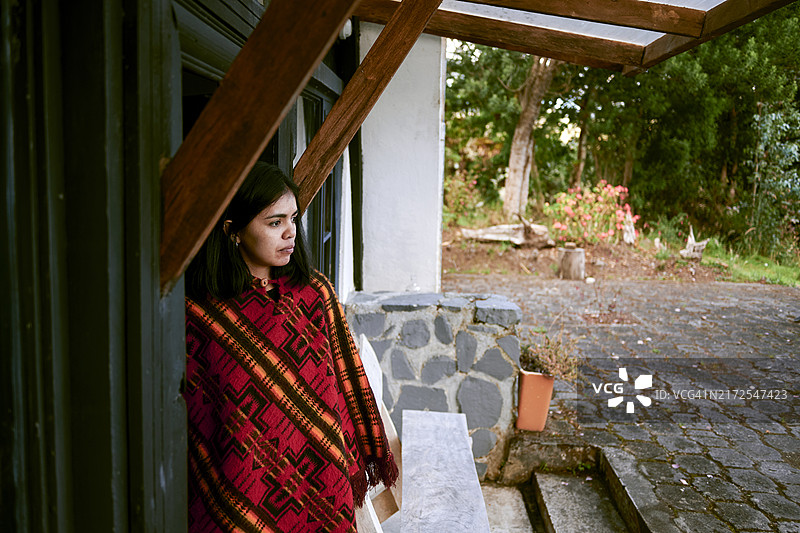 穿着民族披风站在乡间小屋门口的拉丁裔女人图片素材