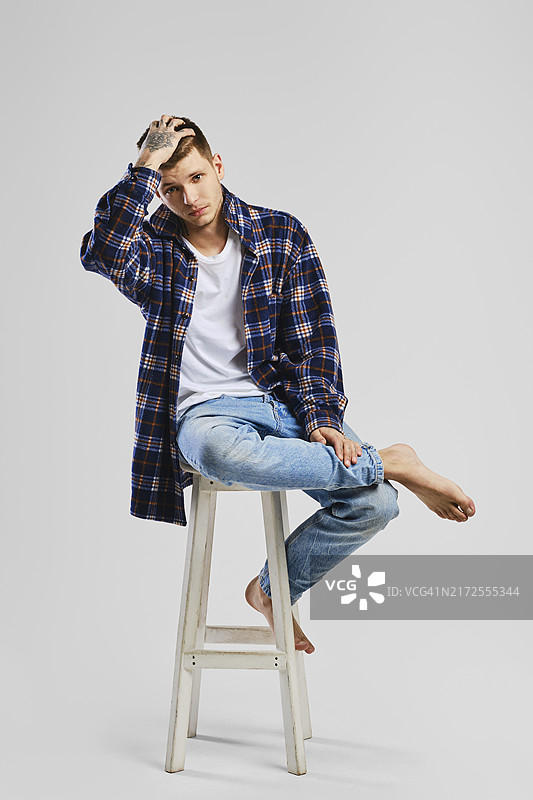 年轻男子衬衫牛仔裤坐高脚椅全身照图片素材