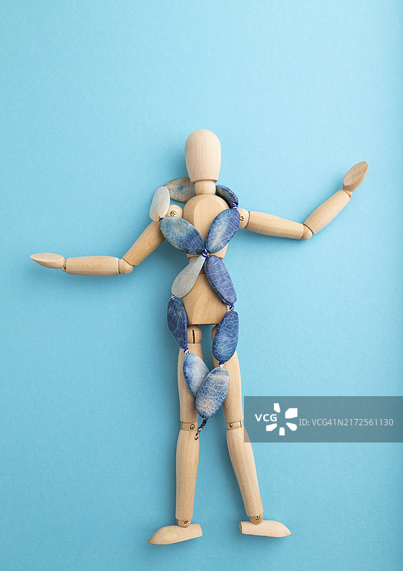带有蓝色玛瑙珠的木制人体模型在蓝色粉彩背景上，有复制空间图片素材