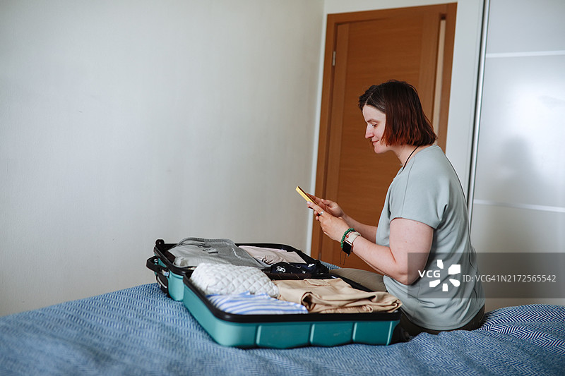 中年妇女在出租公寓的床上用智能手机计划旅行图片素材