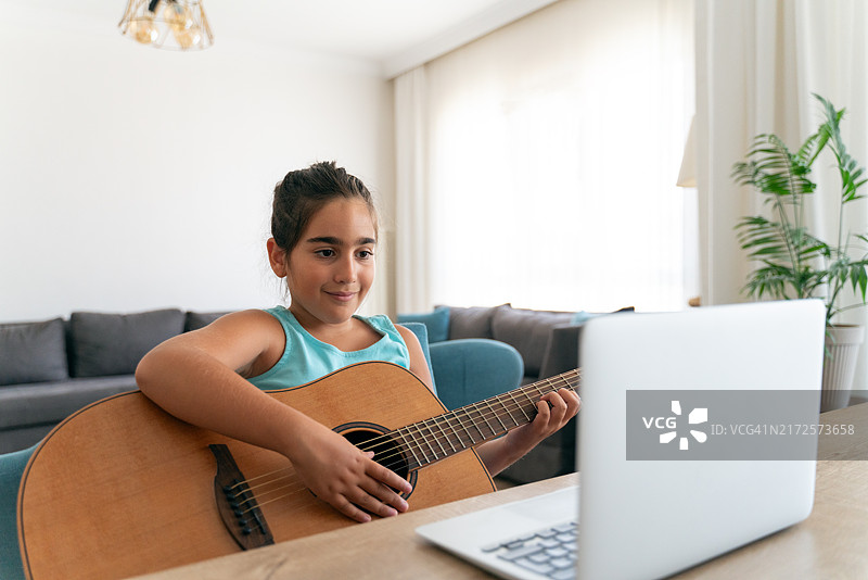 小女孩在笔记本电脑前练习在线吉他课程图片素材