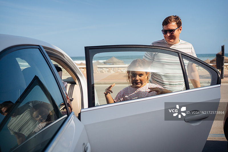 父亲和孩子在阳光明媚的日子里坐在车内，靠近海边。图片素材