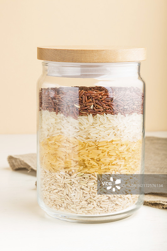 分层倒入不同种类大米的玻璃罐，白色和橙色背景，侧视图，特写，健康食品概念图片素材