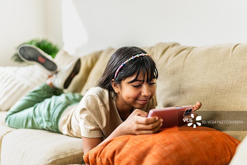 小女孩在家用手机看视频或玩手机游戏图片素材