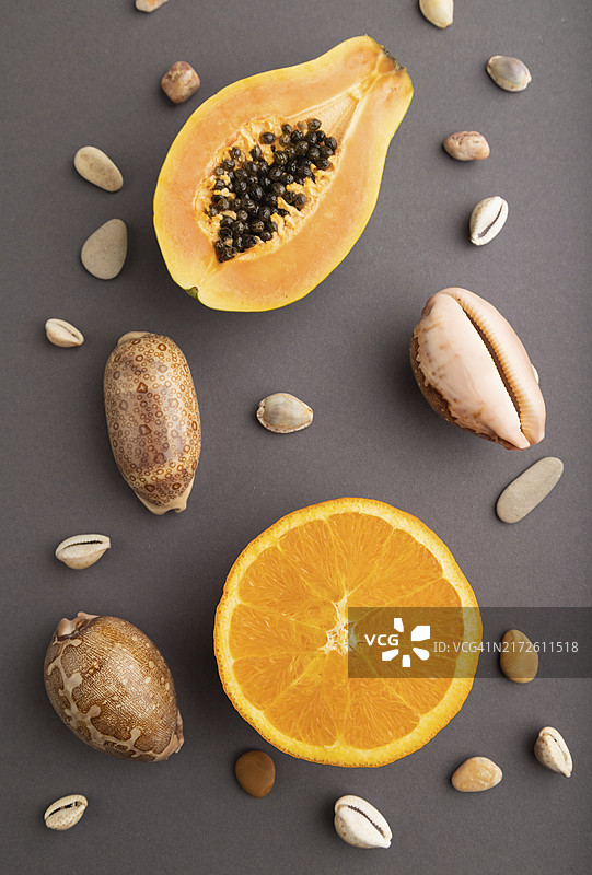 灰色背景上的成熟木瓜、橙子和贝壳，俯视特写图片素材