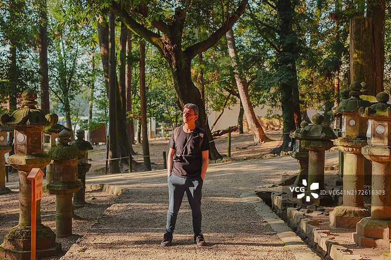 中年游客站在日本奈良的石灯笼之间，手持相机图片素材