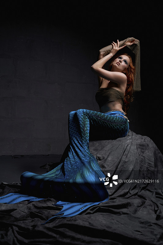 美人鱼坐在水下岩石上，双手伸向水面图片素材