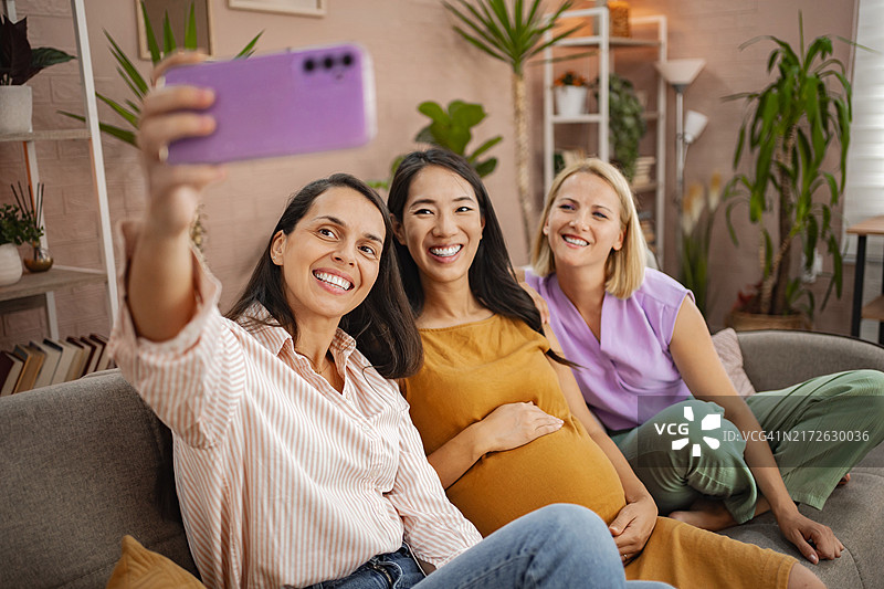 朋友们在舒适的客厅里庆祝准妈妈，充满绿色和温暖的微笑图片素材