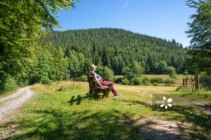 德国黑森林巴特维尔德巴德，坐在长椅上欣赏森林徒步小径的女人图片素材
