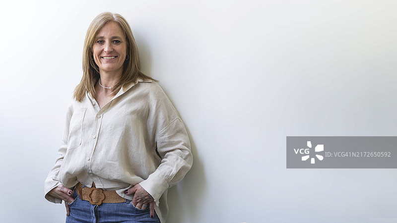 漂亮的白人中年妇女看着镜头靠在白墙上。留白图片素材