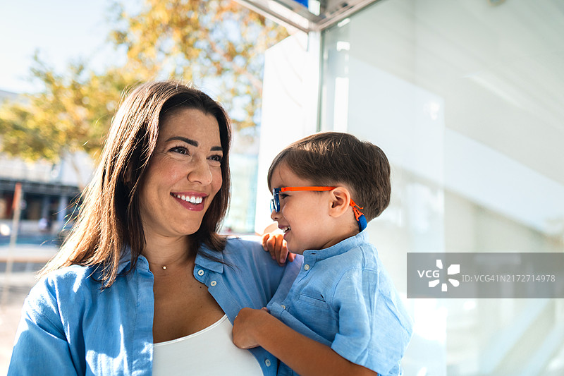 快乐的母亲在户外抱着戴眼镜的微笑儿子图片素材