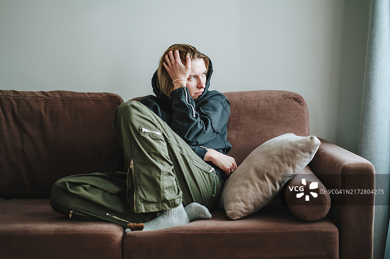 悲伤中的孤独：独自坐在沙发上，凝视窗外，几乎哭泣的沮丧女人图片素材